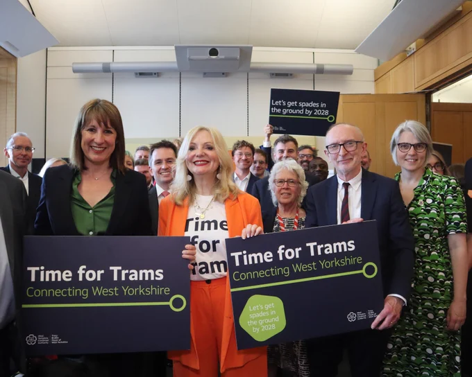 A group of people, stood, smiling. They are holding signs that say Time for Trams, Connecting West Yorkshire
