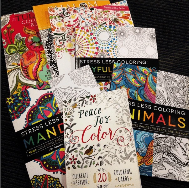Photo of different adult coloring books and colored markers and crayons spread on a table. 
