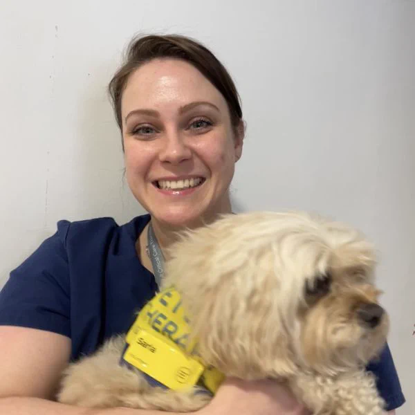 Photo of a Kerry, an NHS staff member holding a therapy dog. Kerry is smiling towards the camera.