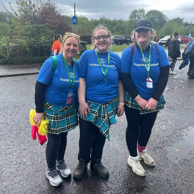 Three people stand together smiling. They are wearing blue Visibility Scotland t-shirts and kilts. 
