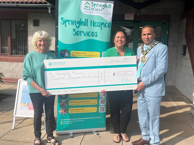 Councillor Tricia Ayrton, deputy leader and portfolio holder for climate change and environment, Jo Ali, community engagement officer at Springhill Hospice, and Mayor of Rochdale, Councillor Shakil Ahmed, holding a large cheque outside Springhill Hospice.