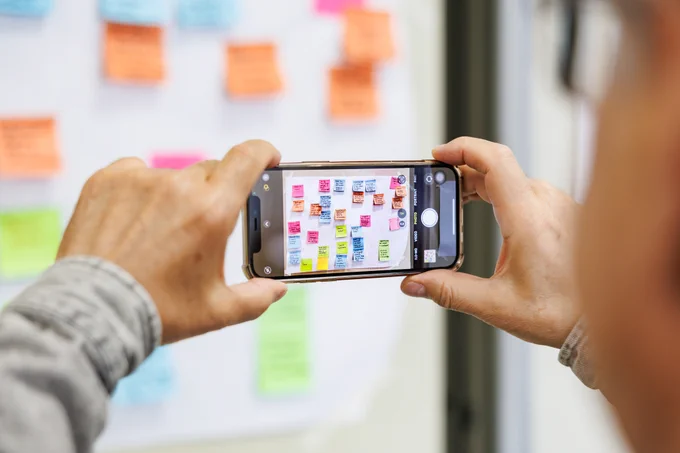 Hands holding iPhone to take photo of sticky notes on wall