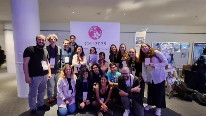 A group of 20 peoplw from lisbon in front kd the CHI 2025 banner