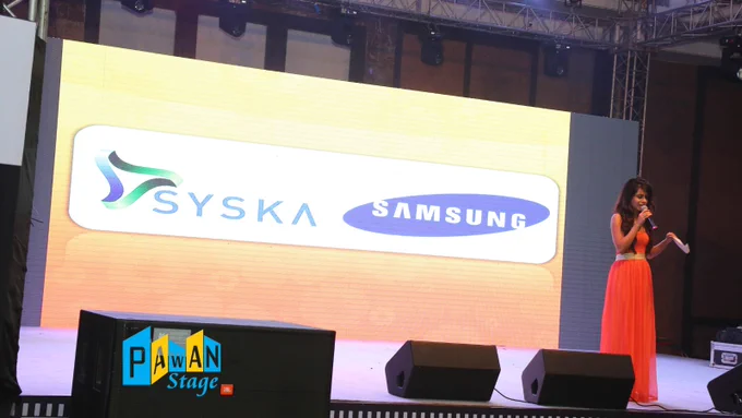 An Anchor stands on stage at a Syska -Samsung product launch event in Udaipur, with the LED Wall on stage.