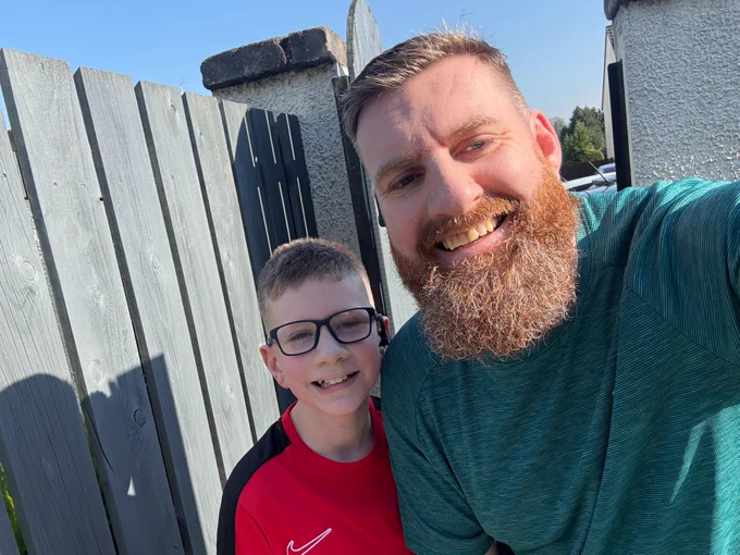 
Image is a sunny selfie of Darren with his trademark beard and his son in their running clothes.
