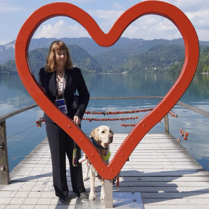 Otto and the Ambassador in front of Lake Bled. They are posing inside a heart-shaped photo frame on a wooden decking. There’s the beautiful Lake Bled and the mountains behind them.