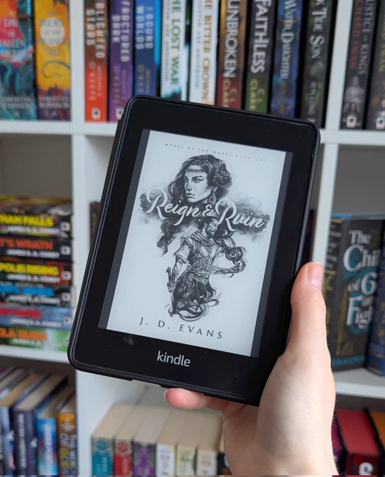 A Kindle being held in front of a bookshelf, showing the cover of Reign & Ruin by J. D. Evans 