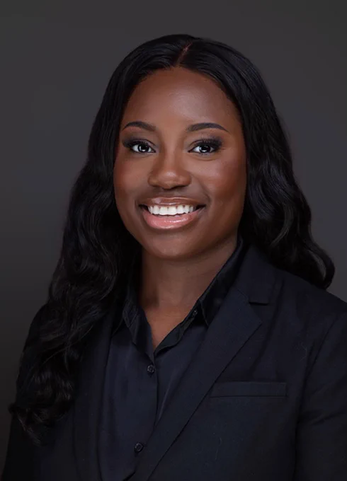 Portrait of a smiling person in a black suit against a dark background.