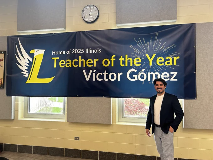 Victor Gomez poses in front of a large banner announcing that he's Teacher of the Year