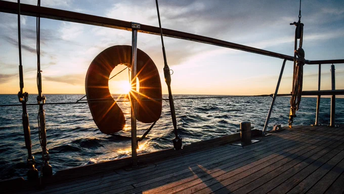 Deck of a yacht with a life saving ring attached to a rail. Yacht sailing on the sea at sunset.
