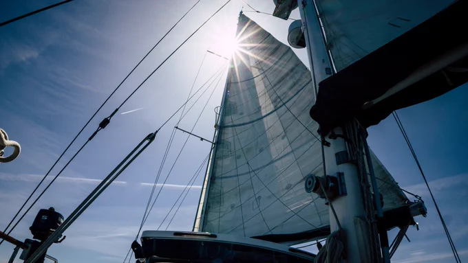 Looking up to a mast and a sail on a yacht with a blue sky background.