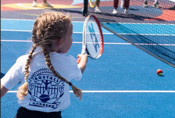 A child with long hair in braids hitting a tennis ball with a racket on a blue court