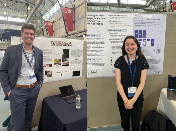 A young man and woman standing in front of posters at a student symposium