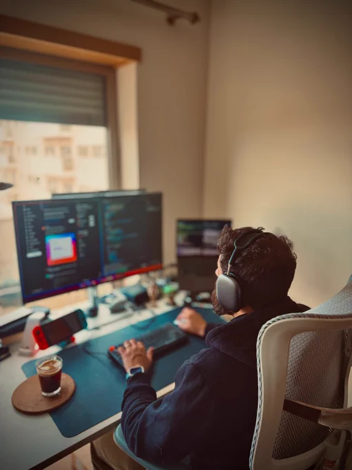 A picture of me sitting in front of my computer, working with my AirPods max listening music and a coffee cup 