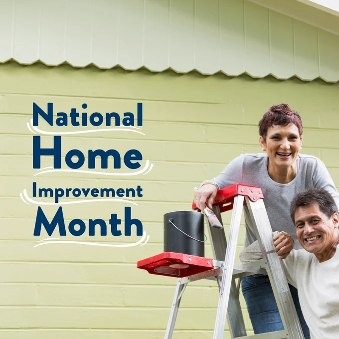 Two individuals smiling while painting a house, celebrating National Home Improvement Month.