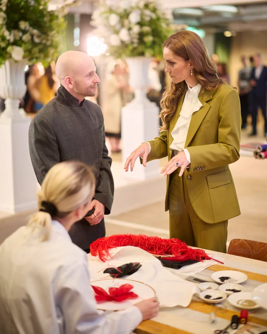 Patrick McDowell and the Princess of Wales talking next to a table with red feathers and tools, with a person seated in front of them.