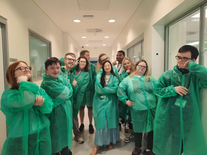 A group of students and staff from TCPID with colleagues from ICON in a laboratory. All are wearing green lab coats, apart from the ICON laboratory supervisor who is wearing a white lab coat. 