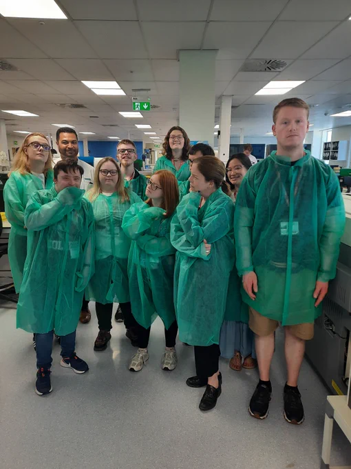 A group of students and staff from TCPID with colleagues from ICON in a laboratory. All are wearing green lab coats, apart from the ICON laboratory supervisor who is wearing a white lab coat. 