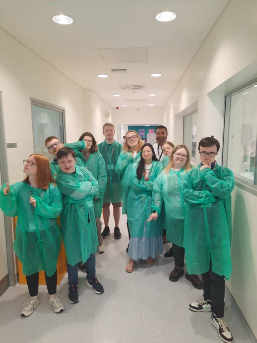 A group of students and staff from TCPID with colleagues from ICON in a laboratory. All are wearing green lab coats, apart from the ICON laboratory supervisor who is wearing a white lab coat. 