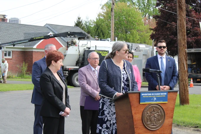 EFC President and CEO Maureen A. Coleman speaks at a podium, flanked by dignitaries in the middle of a street in a residential neighborhood.