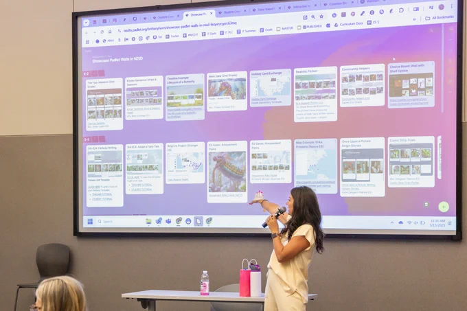 A Northwest ISD presenter is engaging with an image on a large screen in a conference room. Several attendees are visible in the background.