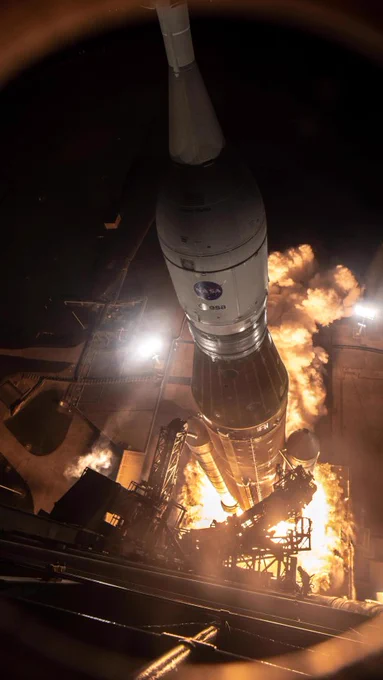 A bird’s eye view of the Artemis I Moon mission's orange-and-white SLS rocket lifting off of its launch pad. Bright flames and billowing smoke emerge from its base as the engines fire. Credit: NASA