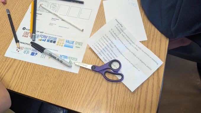 A table with scissors, a sharpie, colored pencils, and paper