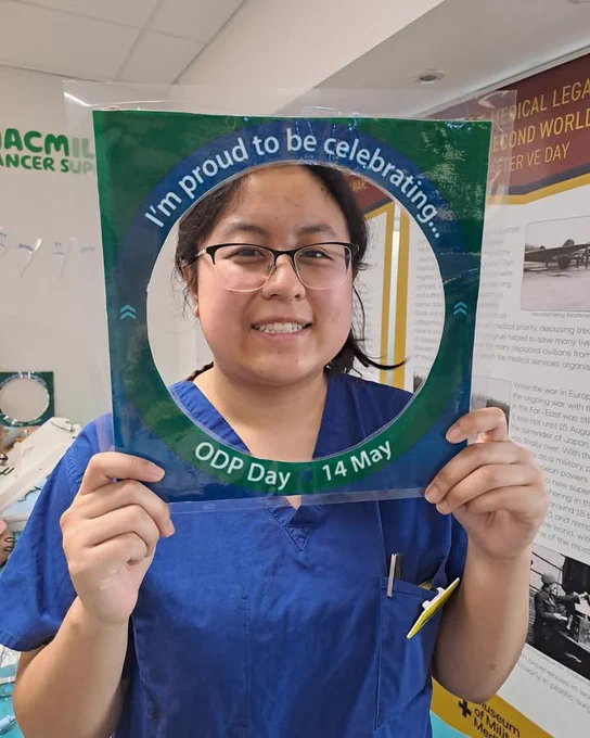 Person in blue scrubs holding a green circular sign that reads "I'm proud to be celebrating ODP Day • 14 May.