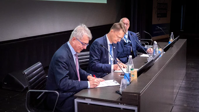 The picture of 2 white men signing a document while a third one is looking at them