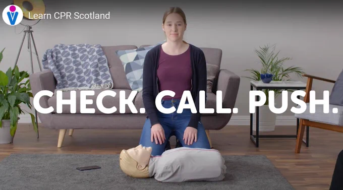 An image of a young person kneeling on the floor of a living room, with a CPR training manikin in front. The Save a Life for Scotland avatar logo in top left corner with wording: Learn CPR Scotland. Across the middle of the screen text that reads: Check. Call. Push.