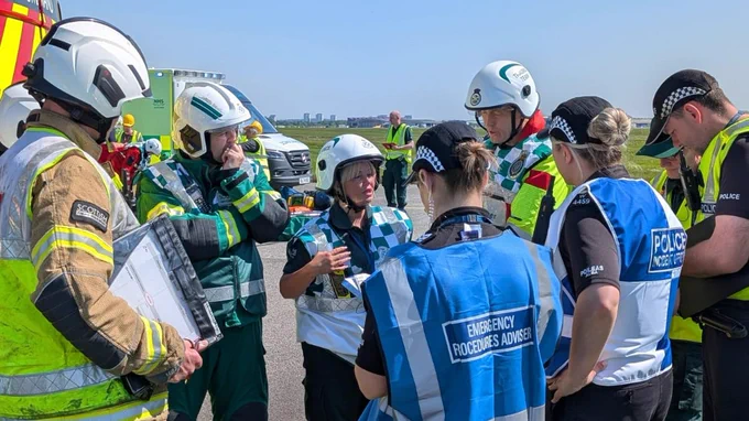 An image of police officers, fire fighters, and ambulance staff standing in a circle engaged in discussion.