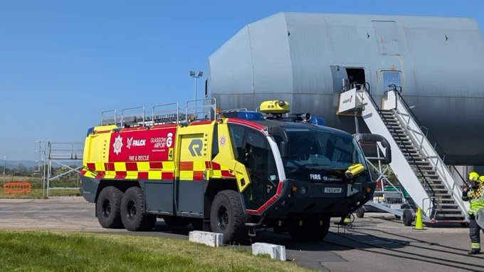 An airport fire engine parked next to a mock training aircraft.