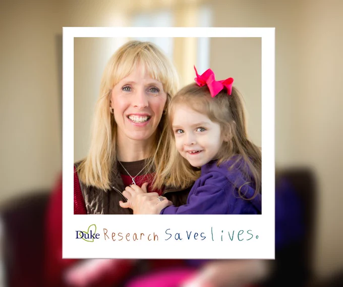 A smiling woman and a young girl are posing together. The woman has long blonde hair and is wearing a black top. The girl, who has brown hair, is wearing a purple dress with a pink bow. The background is blurred, but the focus on their joyful expressions is clear. A caption at the bottom reads, "Duke Research Saves Lives."
