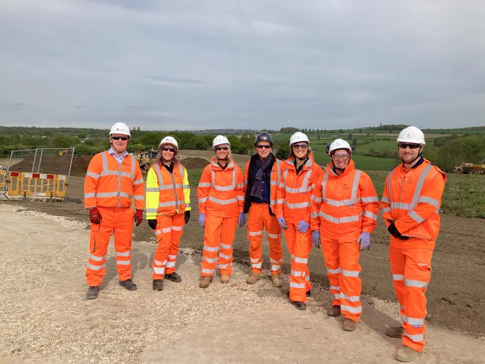 Group of Mining Remediation Authority and Kier colleagues dressed in orange high visibility overclothes in front of an area where topsoil has been stripped ready for construction