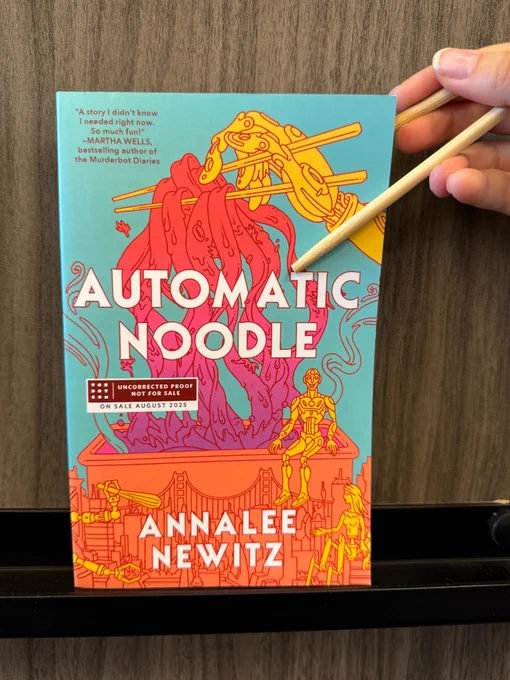 A copy of Automatic Noodle by Annalee Newitz being held by someone with a pair of chopsticks.