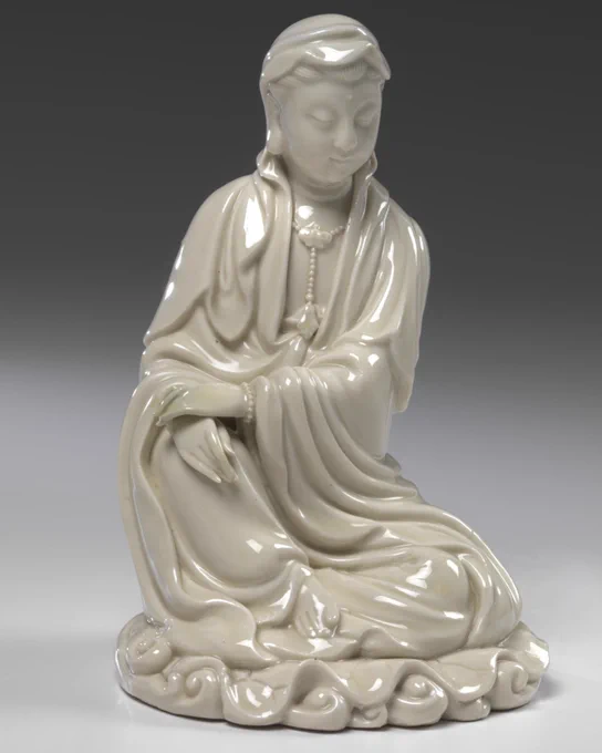 A white porcelain statue of a seated figure wearing a long flowing garment.