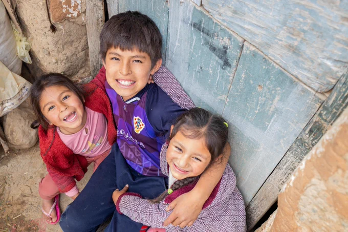 Three smiling children huddled together outdoors, one wearing a Barcelona FC jersey.
