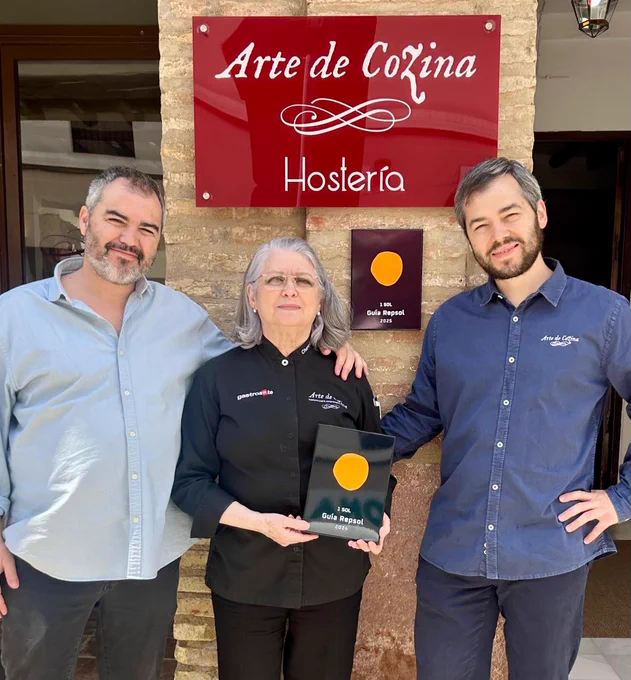 Charo Carmona y sus hijos Luis y Fran posan delante de la entrada de Arte de Cozina con el Sol Repsol 2025 recién colocado.