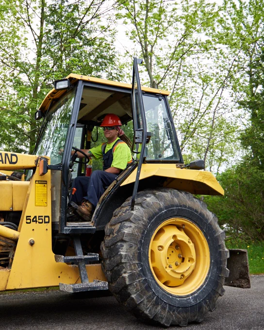 A park staff operating a yellow tractor on a tree-lined path.