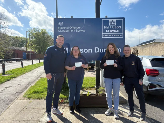 Prison staff stood outside the prison smiling and holding cheques for the amount of money raised for charity