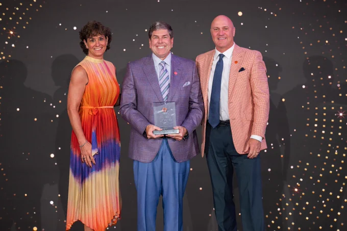 President Clements posing for a photo with two people on a stage.