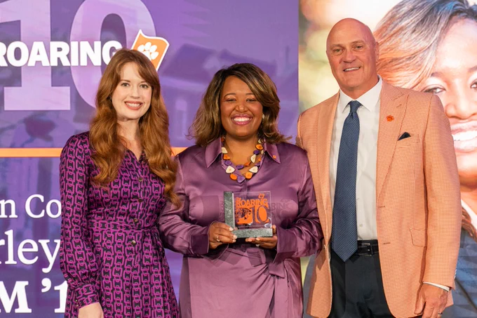President Clements posing for a photo with two people on a stage.