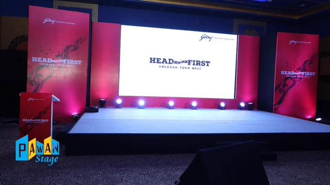 Udaipur corporate event stage with a vibrant red backdrop and a large screen for visual displays.