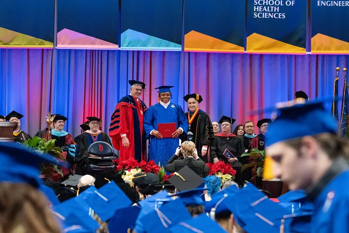 Graduate Charles Harris, center, gets his photo taken on the Commencement stage with President Ken Gormley, left, and the Health Sciences dean, right. 