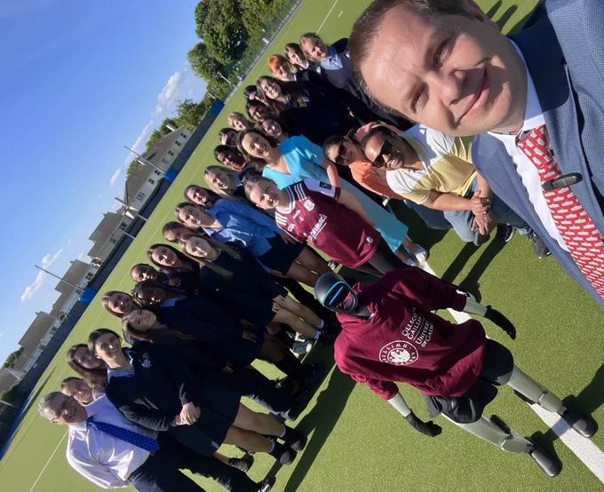 Humanoid Robot Deckard wearing a University of Galway hoodie, standing in the middle of a group of students & researchers from the HIVE Lab