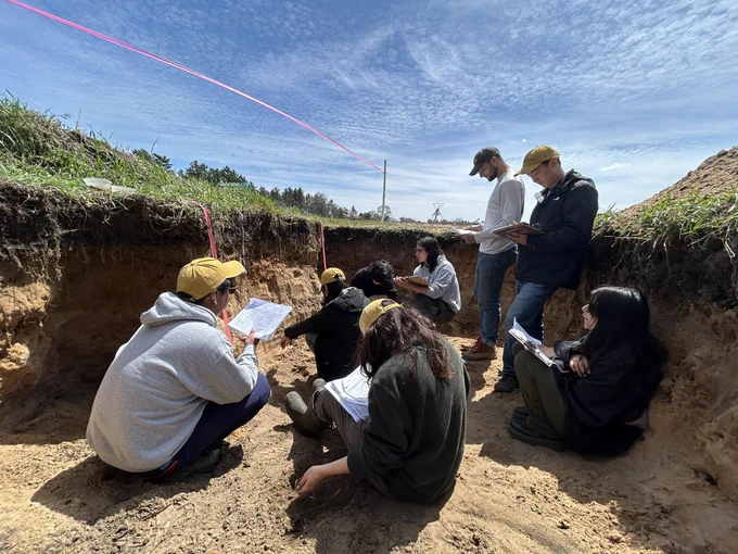 Students and coaches go over soil characteristics inside soil pit