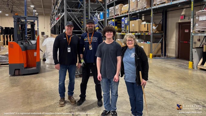 A group photo of four of the volunteers smiling to the camera. The man on the left is wearing a hat, lanyard, and a black long sleeved shirt, then a man with a hat, glasses, beard, lanyard, and LayerZero logo shirt, next a younger man wearing a gray pocket tshirt, lastly an older woman wearing a blue tshirt and jacket. The bottom left hand corner has text that reads, “LayerZero® is a registered trademark of LayerZero Power Systems, Inc. All rights reserved.” The bottom right hand corner has the official logo and below it reads the website name, “www.LayerZero.com”.