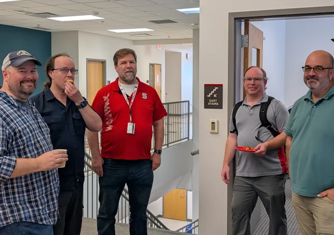 Staff from various OIT units pause for a photo while one staff member eats a doughnut.