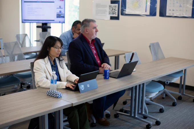 [ID: Pictured is a photo of people listening to a presentation during a workshop in the Day Family Research Lab.]