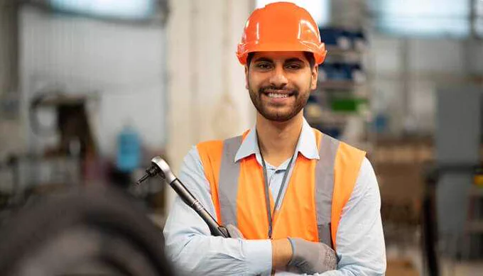 Smiling Smart Worker in safety gear, standing confidently in a workshop, showcasing the blend of human skill and advanced technology for enhanced productivity.